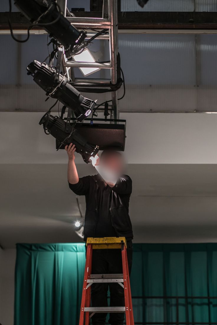 Crew member focusing a fixture on a ladder